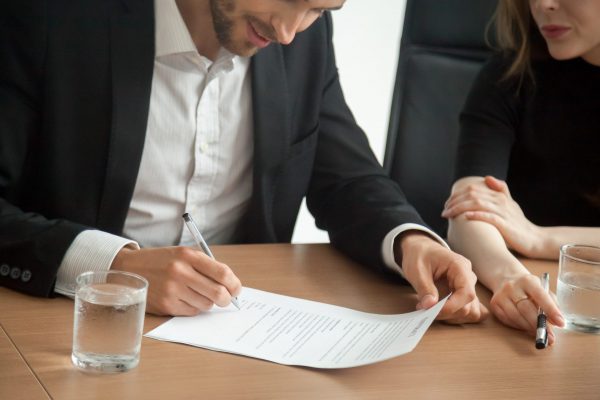 Satisfied smiling businessman in suit signing contract at meeting concept, investor or entrepreneur putting written signature on business document making good partnership deal, taking loan insurance